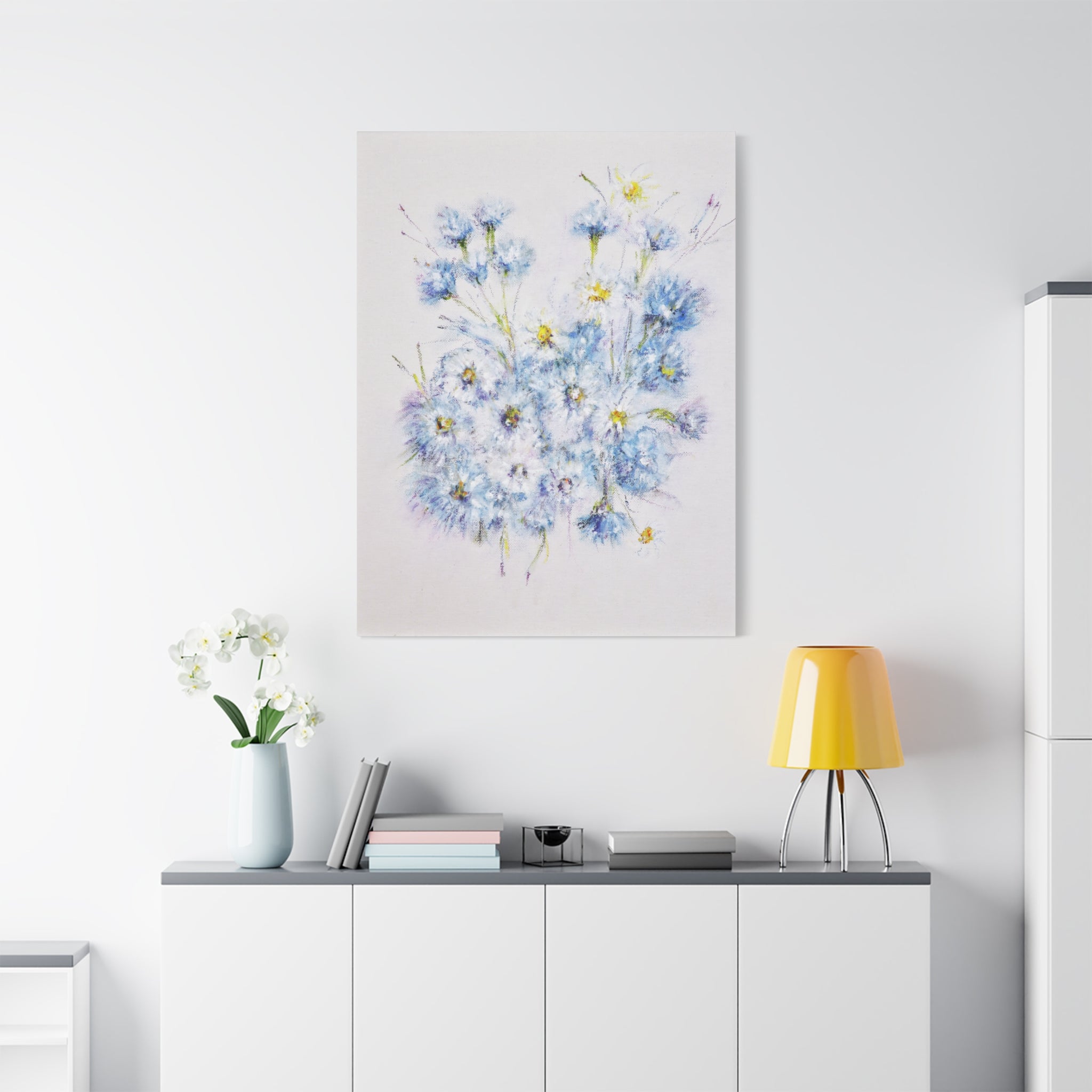 Canvas printed after original oil painting of blue flowers on a wall above a white cabinet with a yellow lamp.