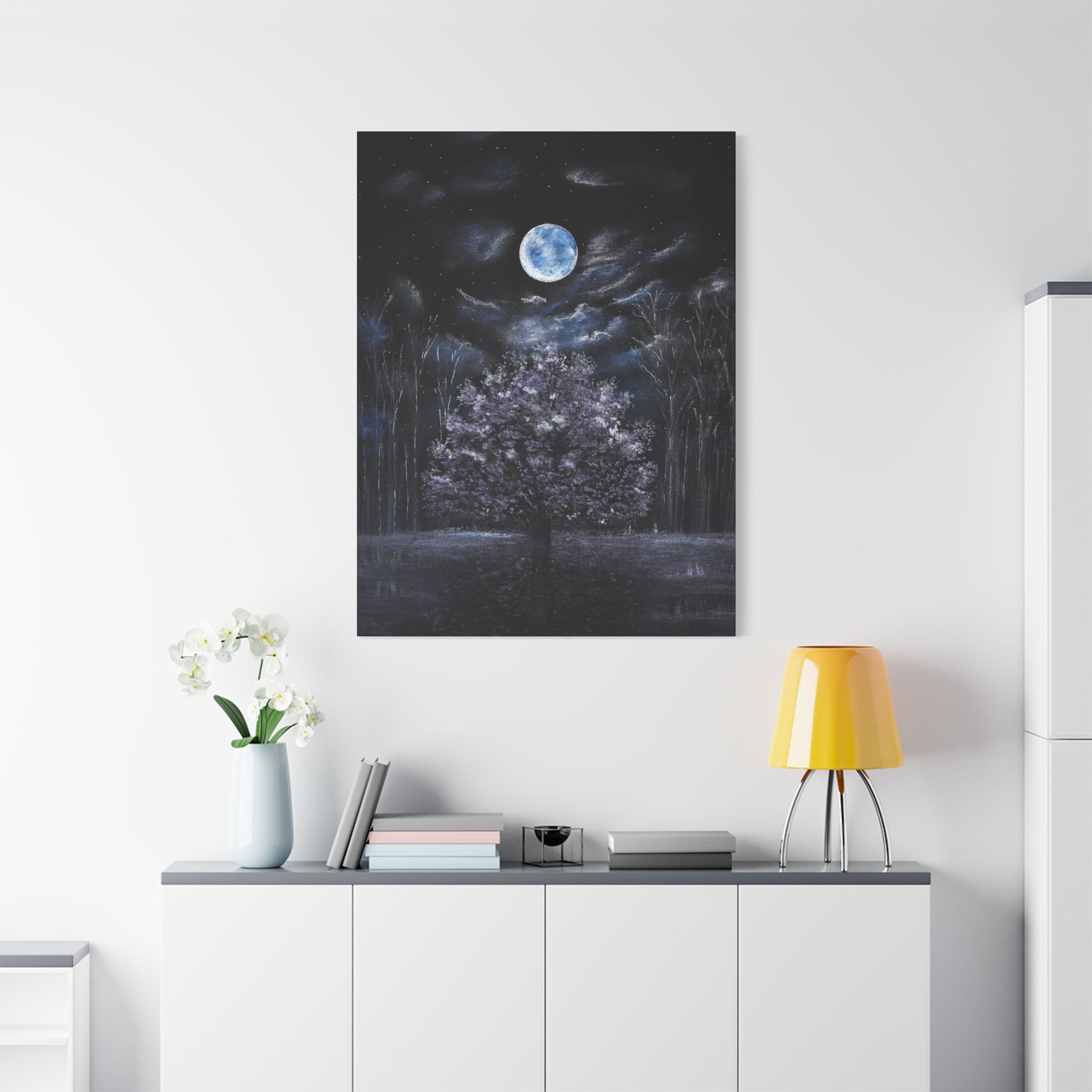 Printed Canvas art of a moonlit forest in white, blue, purple and dramatic shadows, above a white cabinet with decorative items.