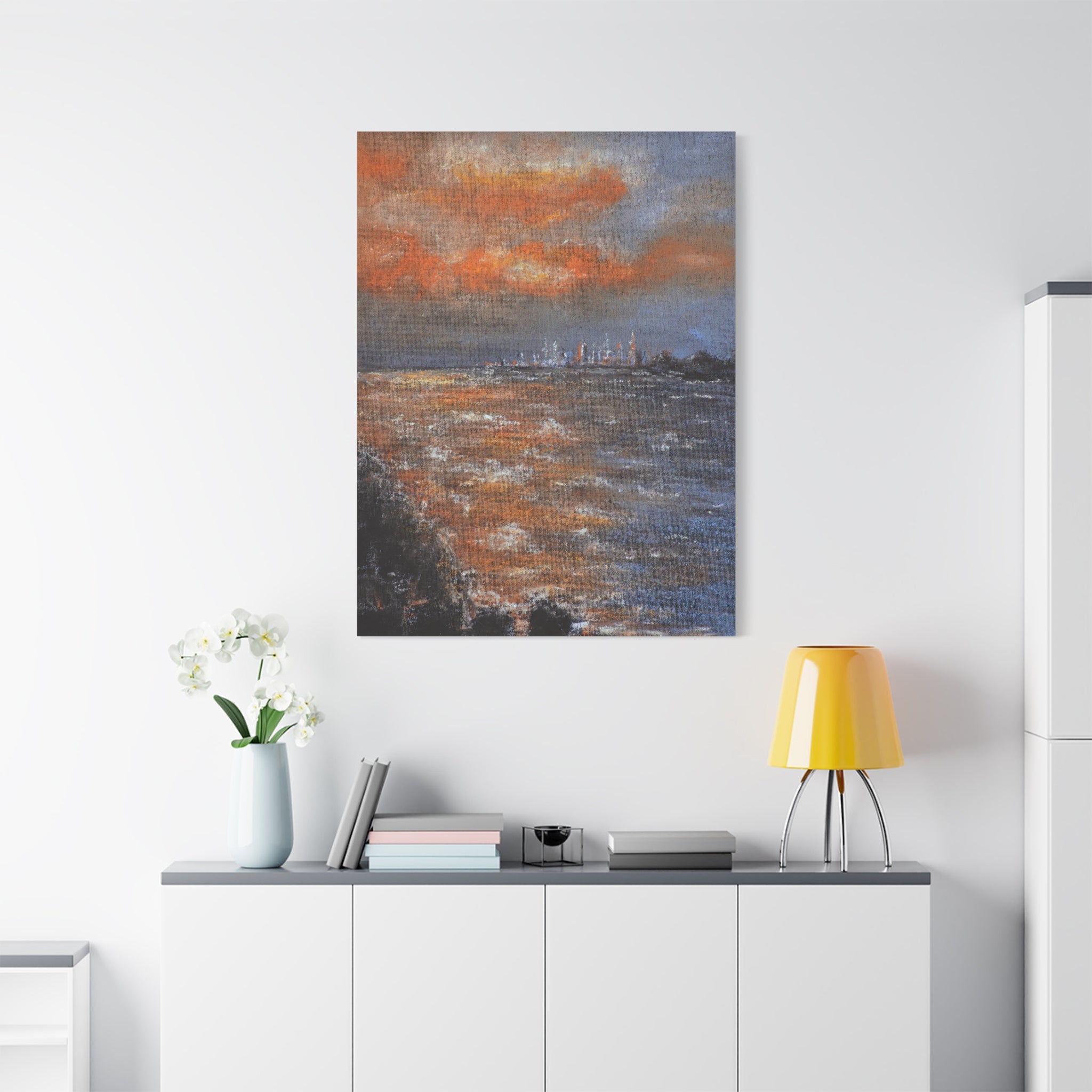 Sunset Coastal Canvas Wall Art after painting of a sunset over water on a white wall above a desk with a lamp and vase.